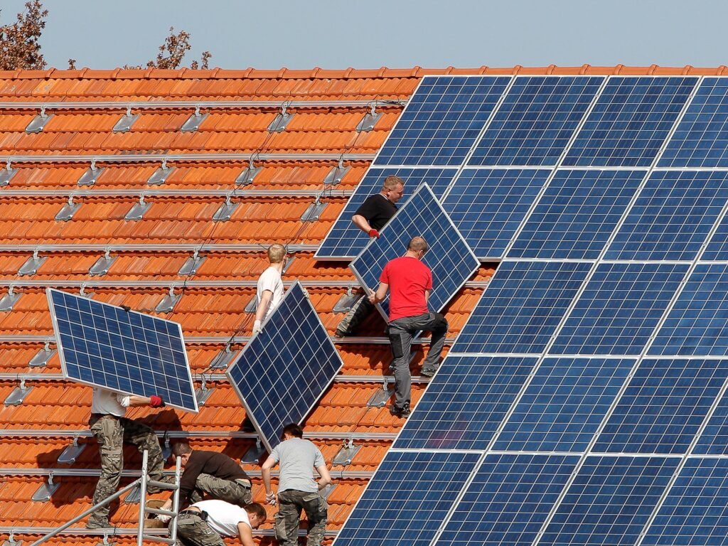 A team of professional installers working on a residential rooftop, carefully lifting and securing solar panels onto the tiled roof.