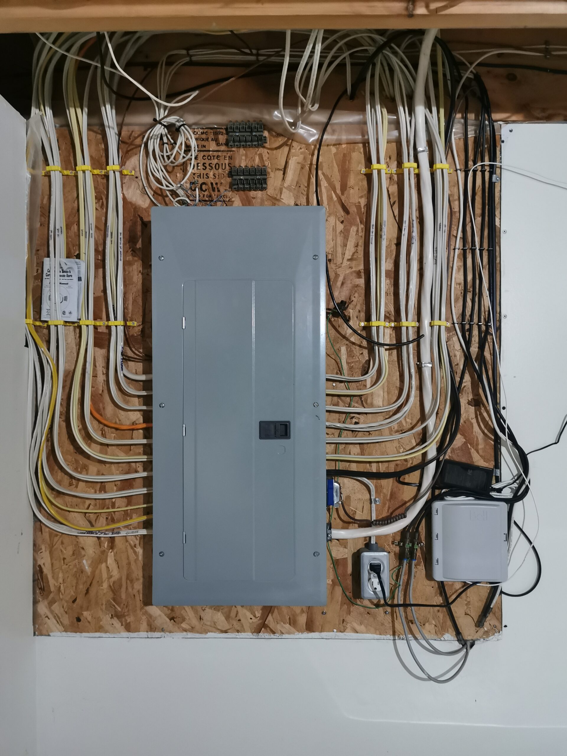 Residential electrical breaker panel with neatly organized wiring mounted on a plywood wall.