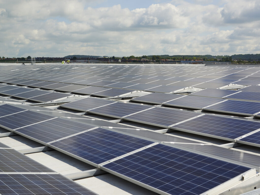 A wide shot of a large commercial rooftop covered in rows of newly installed solar panels under a cloudy sky.