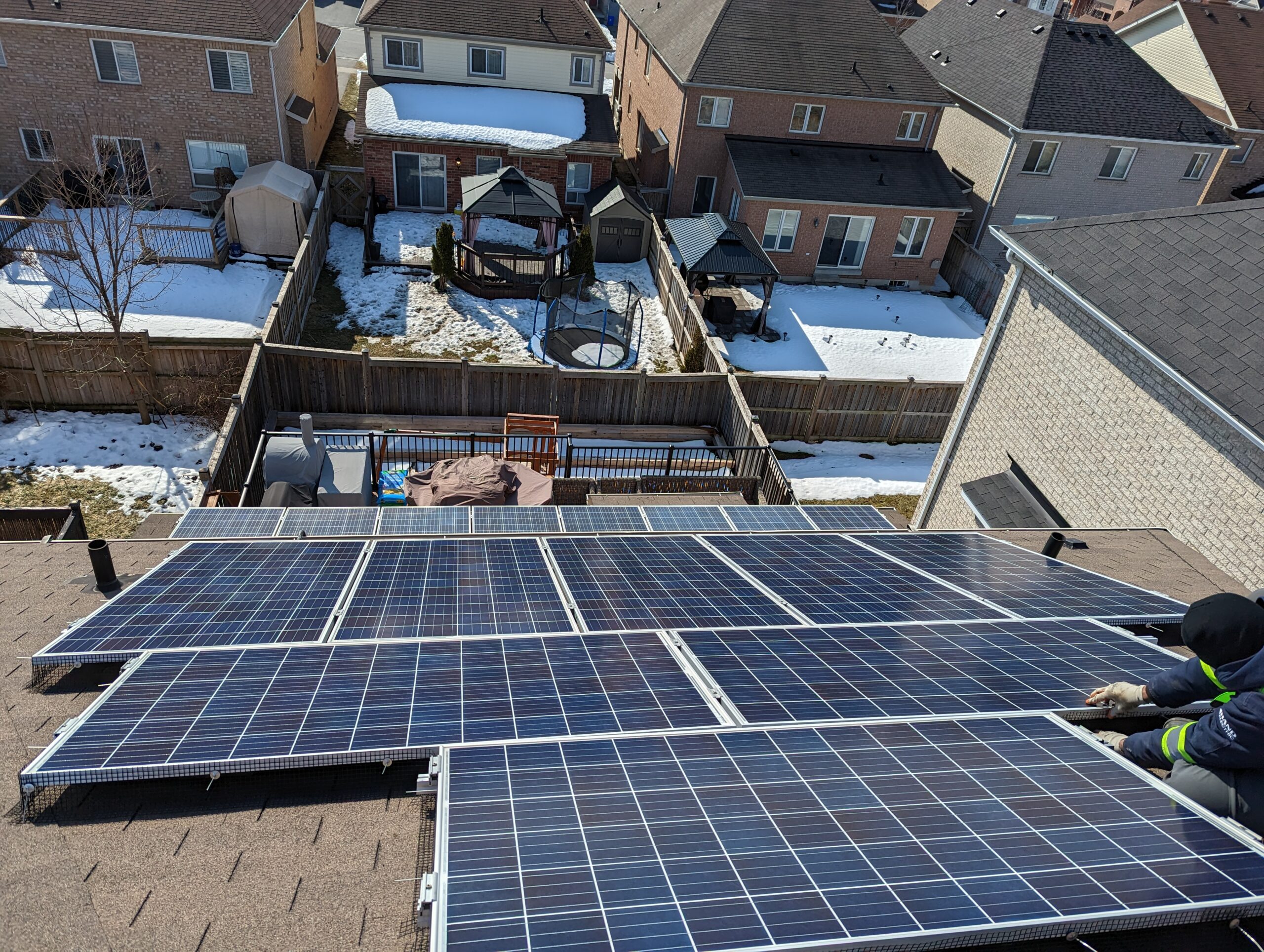 Solar panels being installed on a residential rooftop with a snowy neighborhood in the background.