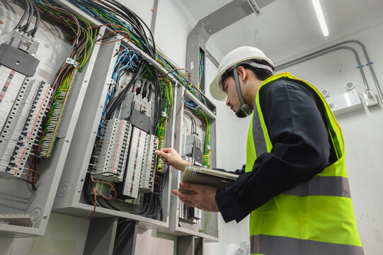 An ENV Electric technician in a safety vest and hard hat inspects wiring within a commercial electrical control panel while holding a tablet for documentation of electrical services.