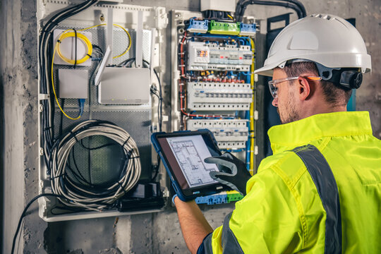 An electrician reviewing digital blueprints on a tablet while inspecting a commercial networking and electrical hub in Durham.