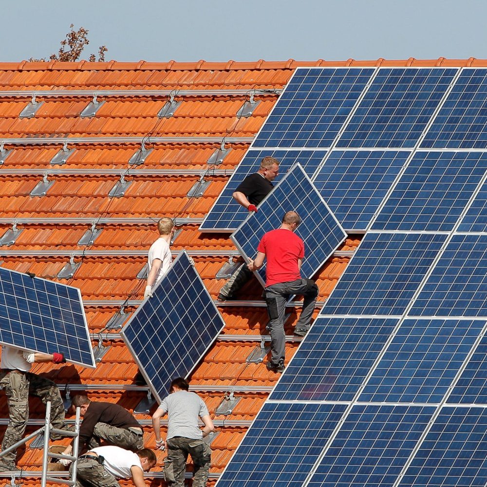 Professional Solar Panel Installation | Rooftop Solar Team A team of professional installers working on a residential rooftop, carefully lifting and securing solar panels onto the tiled roof.