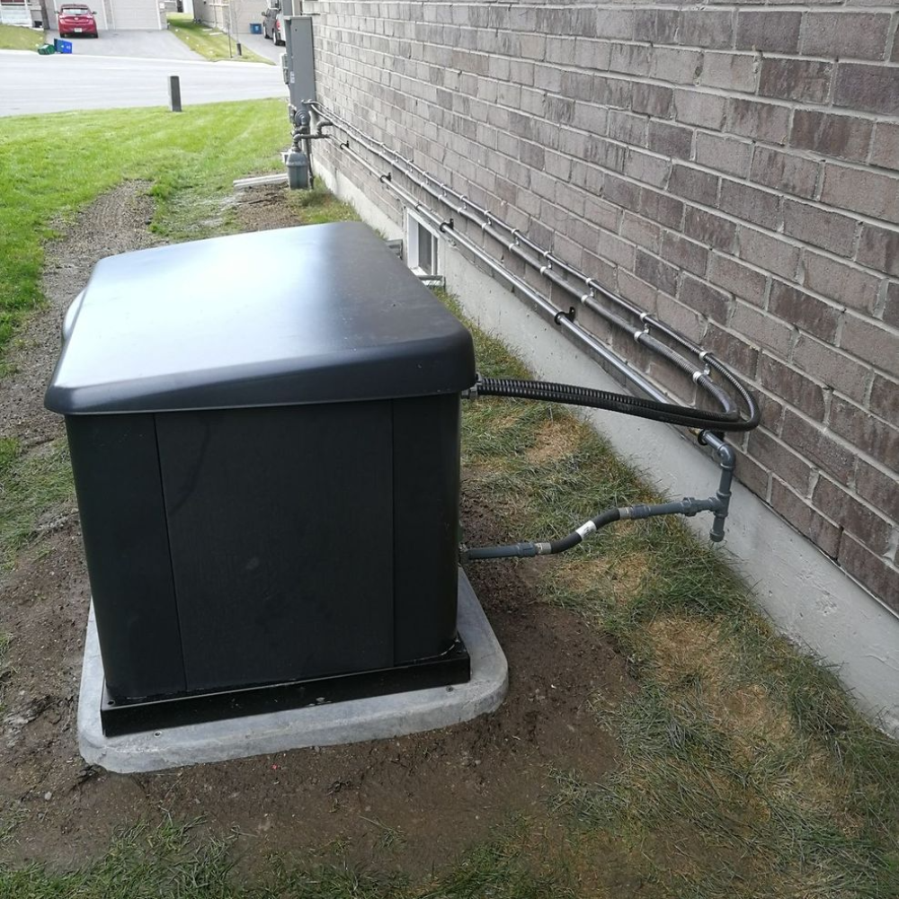 Residential Backup Generator Installation | Home Standby Power A residential standby generator with a black protective cover, installed on a concrete pad next to a brick house.